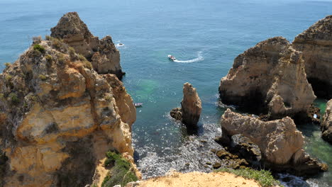 ponta de piedade, portugal, boat sailing between scenic limestone rock formations on sunny summer day