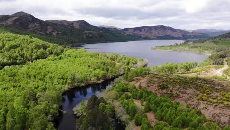 Aerial-rising-shot-showing-a-Sottish-Loch,-Mountains-and-Forest-bathed-in-sunlight