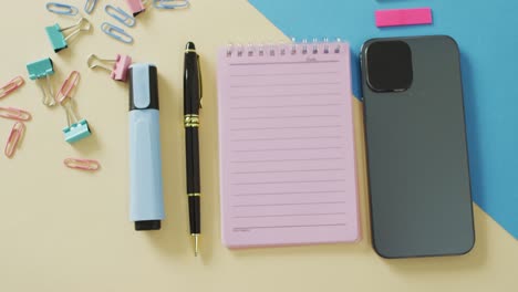 video of smartphone, notebook with copy space and school equipment on yellow background