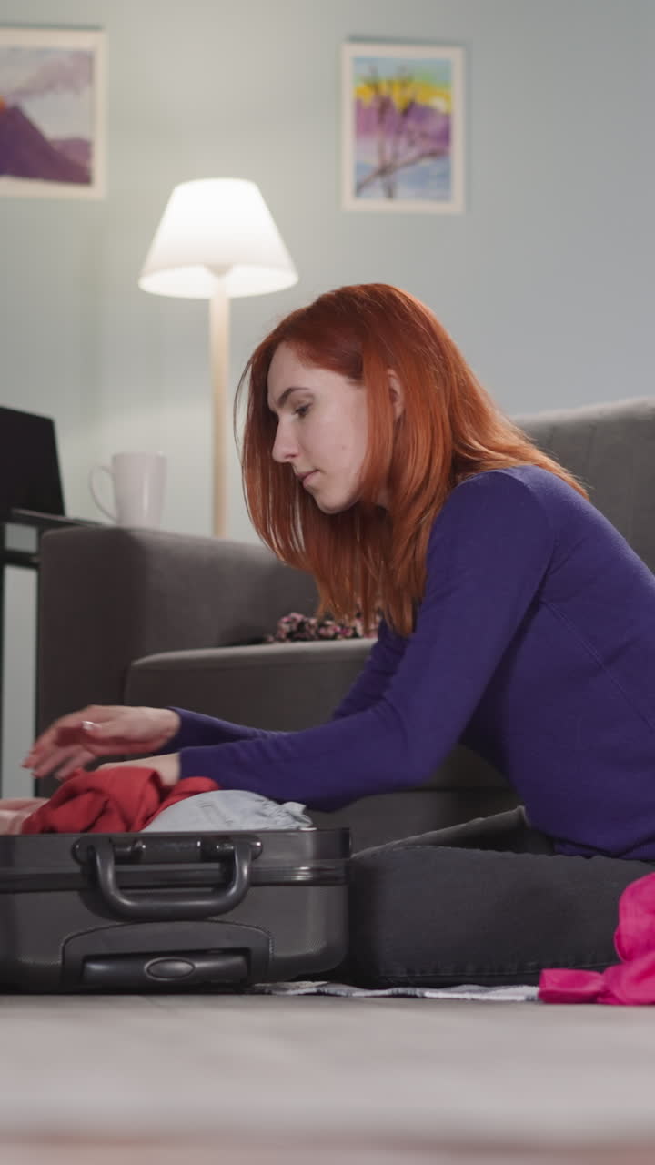 mujer enfocada con cabello rubio desmonta las cosas sentada en el suelo en casa. ama de casa saca la ropa de la maleta abierta después de las vacaciones en cámara lenta