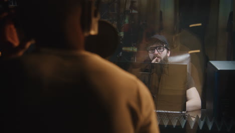 vocalist sings composition into microphone african american vocalist sings composition into microphone in soundproof room experienced audio engineer or producer works with singer in sound recording studio music production concept back view