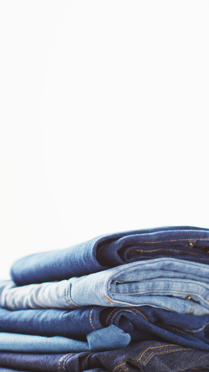 Vertical video of folded jeans with different shades on white background with copy space