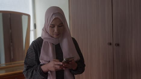 Muslimische-Asiatische-Indonesische-Frau-Im-Hijab-Greift-In-Die-Tasche-Nach-Dem-Telefon-Und-Beginnt-Mit-Dem-Schreiben-Einer-SMS