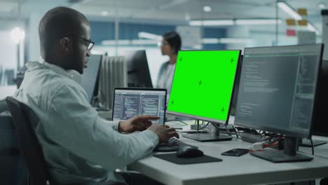 multi-ethnic office: black it programmer working on computer with green screen chroma key display. male software engineer developing app, program, video game. terminal with code language. static shot