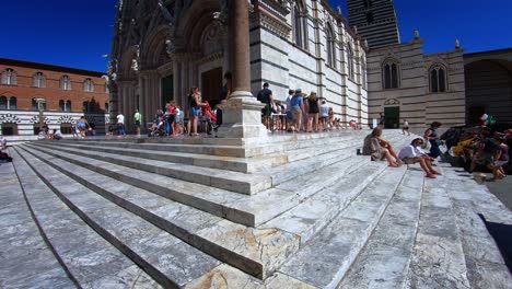 siena, tuscany / italy - circa august 2019 : pan up reveal of tourists in line for a visit to siena cathedral (duomo di siena)