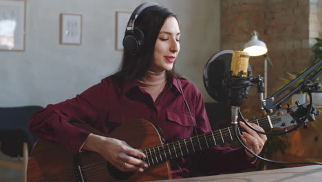 pretty woman playing guitar and talking at camera in recording studio