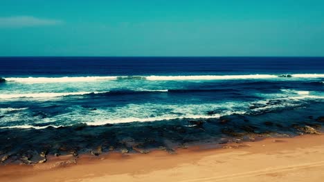 Luftaufnahmen,-Die-Mit-Einer-Drohne-Gefilmt-Wurden,-Mit-Blick-Auf-Den-Strand-Und-Das-Meer-Aus-Tosenden-Wellen-Mit-Einem-Tiefblauen-Ozean-Auf-Der-Klippe-In-Der-Südlichen-Hemisphäre-Afrikas