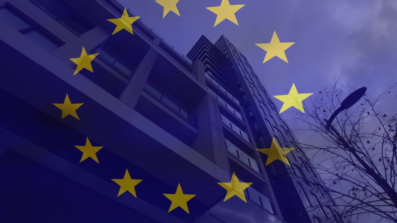 Mentre il cielo crepuscolare si oscura, un anello di stelle dell'UE ruota in senso orario sopra un condominio, mostrando l'unità dell'UE.