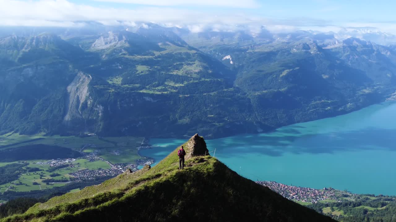 toma aérea de un hombre parado en un acantilado en un día azul claro con vistas al paisaje del lago brienz, cerca de brienzer rothorn y los impresionantes alpes europeos de suiza