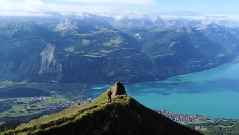 aerial drone shot of a man standing on a cliff on a clear blue day with a view of the scenery of lake brienz, close to brienzer rothorn and the stunning european alps of switzerland