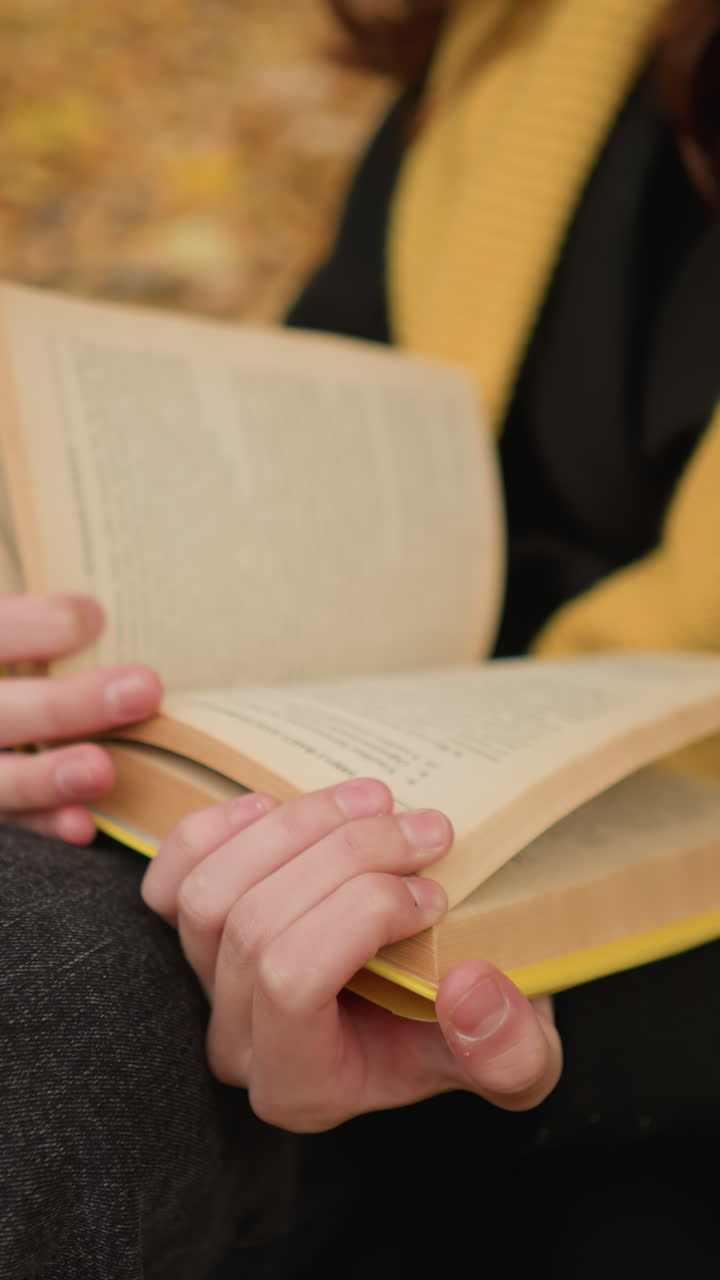 primer plano de las manos hojeando las páginas del libro pensativamente, las hojas de otoño cubren el suelo mientras la persona lee en un entorno pacífico al aire libre, inmersa en el momento con curiosidad y reflexión