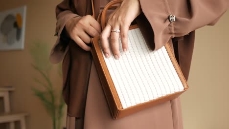 woman in brown abaya carrying a white and brown handbag