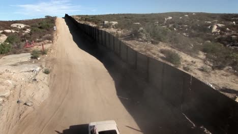 A-car-with-a-flag-drives-down-a-road-behind-a-tall-fence