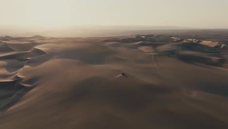 aerial view of dune buggy driving through sand dunes at sunset