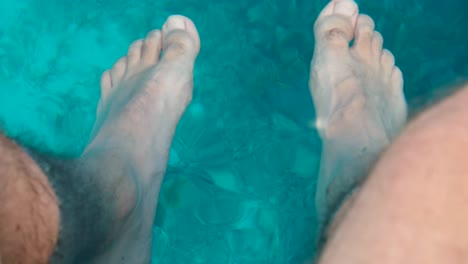 Feet-dangling-into-crystal-clear-ocean-water-cooling-off-and-relaxing-whilst-on-vacation-in-Raja-Ampat,-West-Papua,-Indonesia