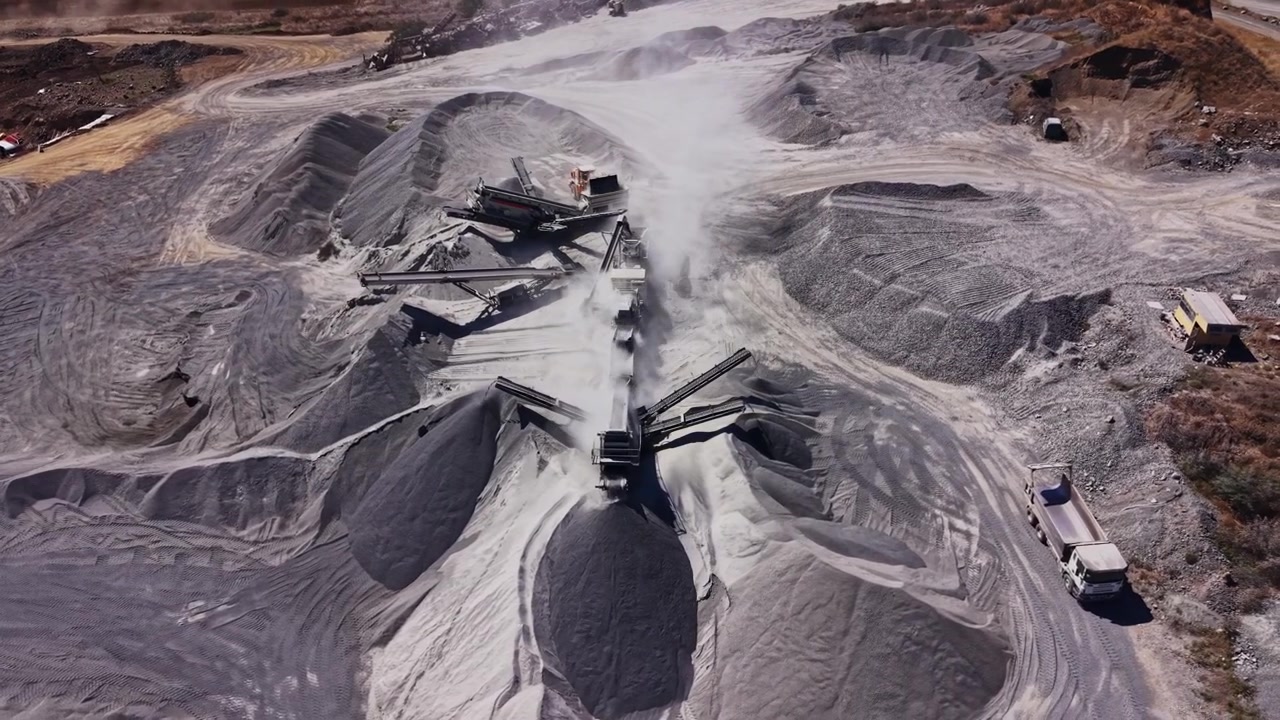 Heavy machinery operates at a construction site with piles of gravel