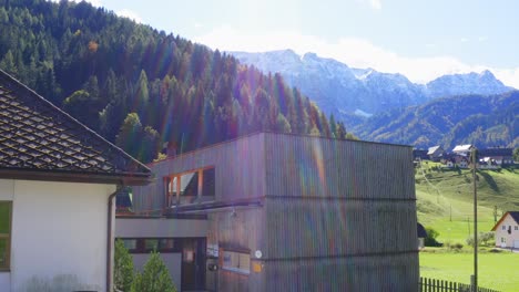 a flyover shot of houses at the valley surrounded by forest and revealing mountain behind it