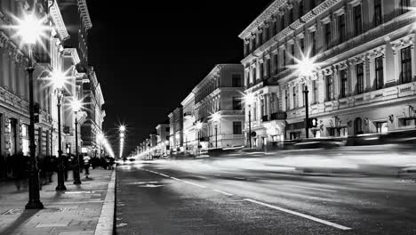 black and white city street at night with blurred car lights, historic buildings, and street lamps