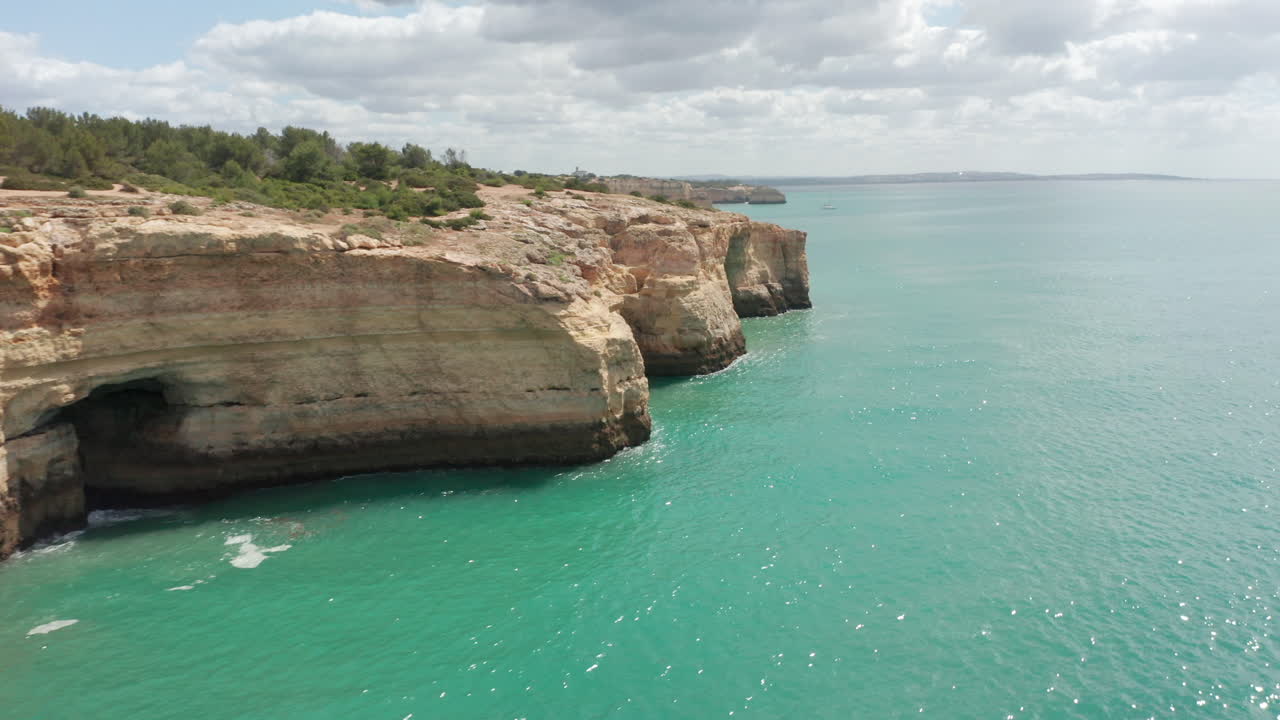 아름다운 바다의 절벽 공중에는 모래 해변이 있는 멋진 숨겨진 동굴이 드러납니다.