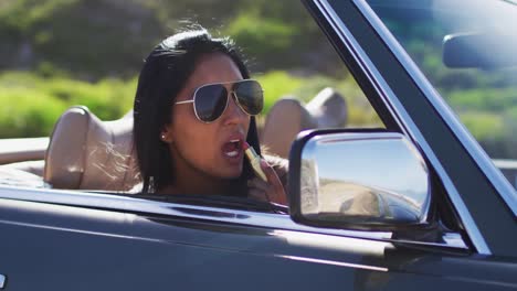 mujer afroamericana aplicando lápiz labial mientras mira en el espejo de un coche descapotable