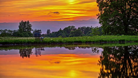 Simetría-En-El-Reflejo-Del-Lago-Del-Asombroso-Cielo-Naranja-Y-La-Zona-Rural