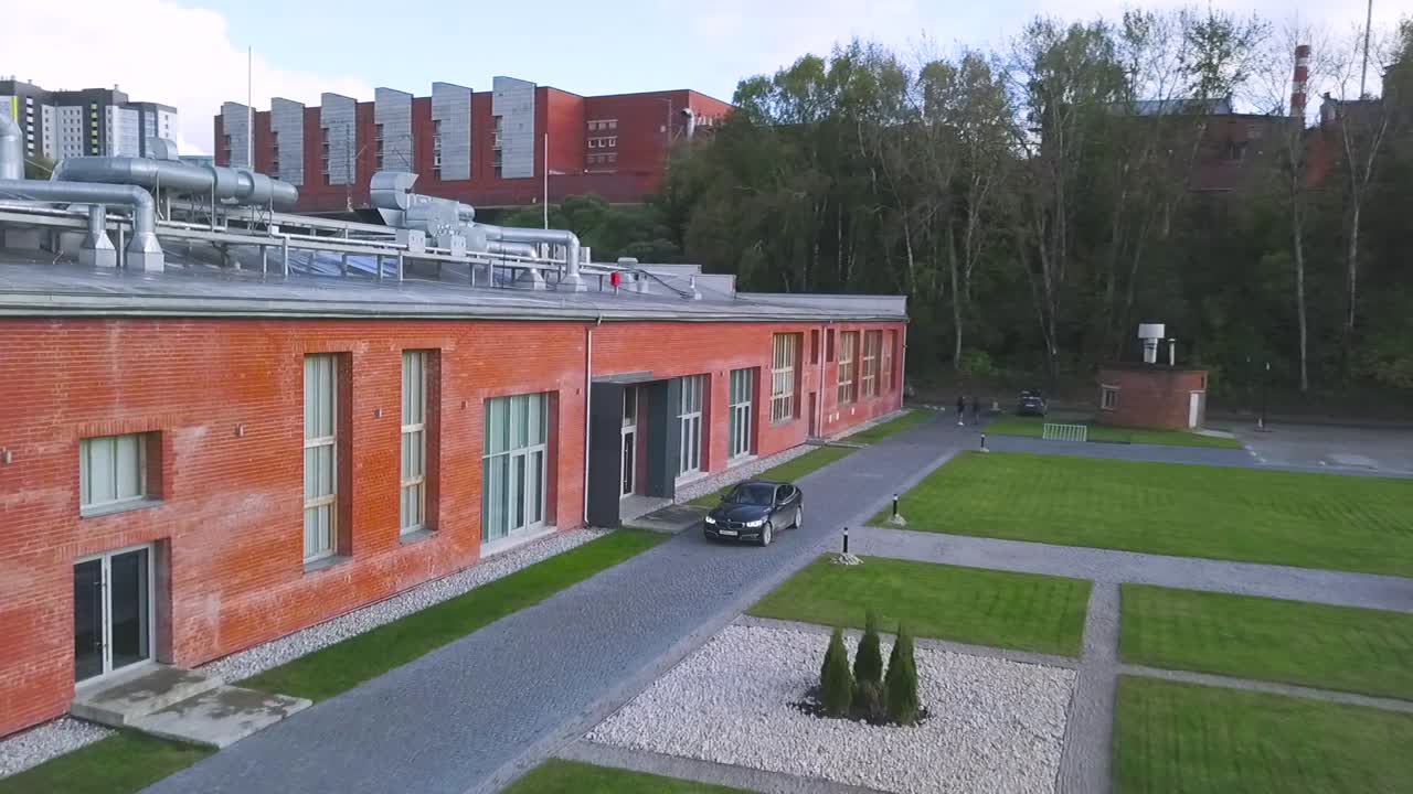 современное кирпичное здание с озеленением и машиной