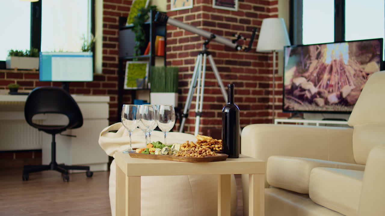 Panning shot of empty cozy apartment living room with appetizer platter and wine bottle on table
