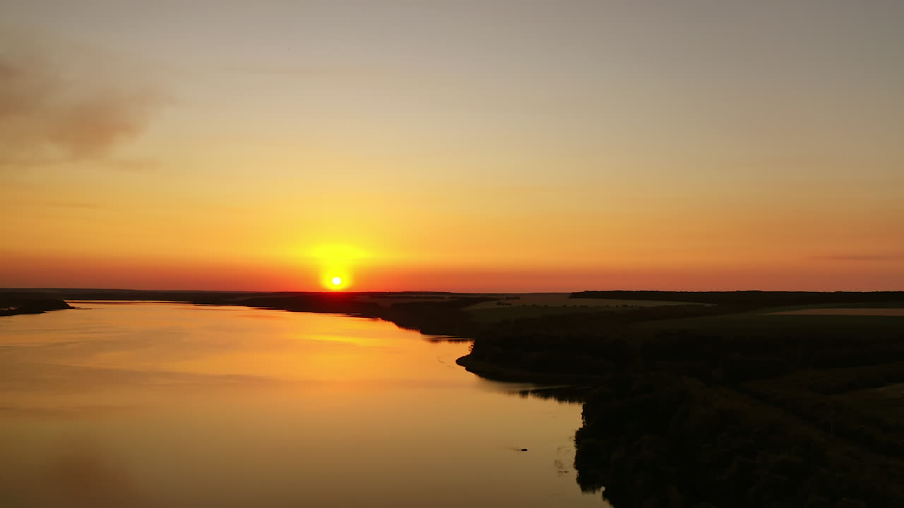 Orange sunset. Beautiful view of river under colorful sky of the setting sun. Amazing sunset on water surface. Aerial view.