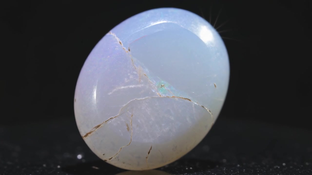 Piattaforma girevole che ruota un cabochon ovale lucidato per rivelarne la traslucenza su un palco da studio, con un lampo verde
