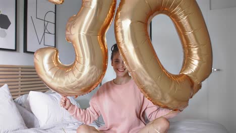 Portrait-of-cheerful-woman-with-golden-balloons-forming-the-figure-'30