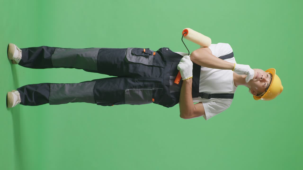 Full Body Of Asian Man Painter Wearing Safety Helmet Thinking About Something And Looking Around While Standing In The Green Screen Background Studio