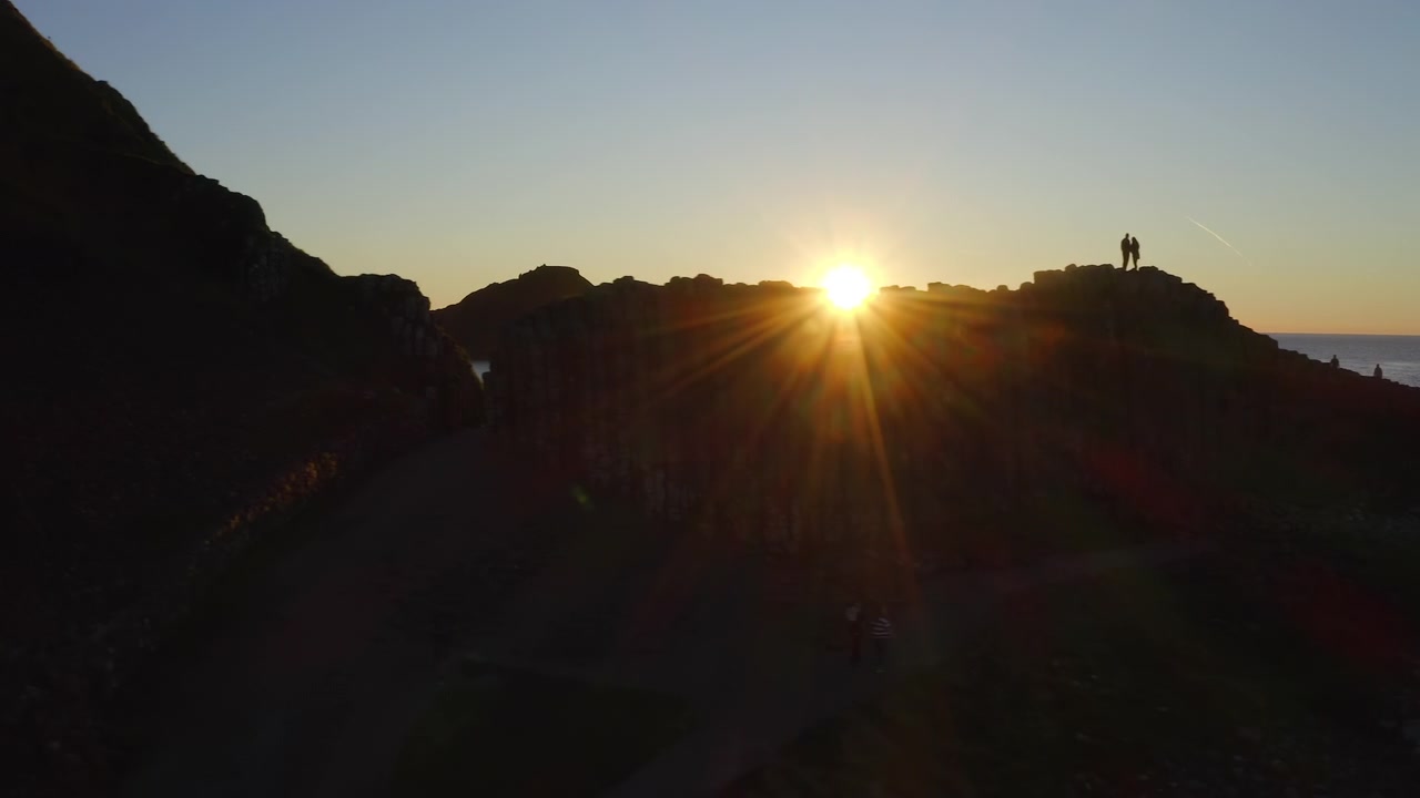 Tourists silhouetted at Giant's Causeway, enjoying a stunning sunset. Aerial pan