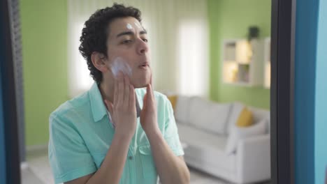 A-well-groomed-boy-is-applying-cream-on-his-face-in-front-of-the-mirror.