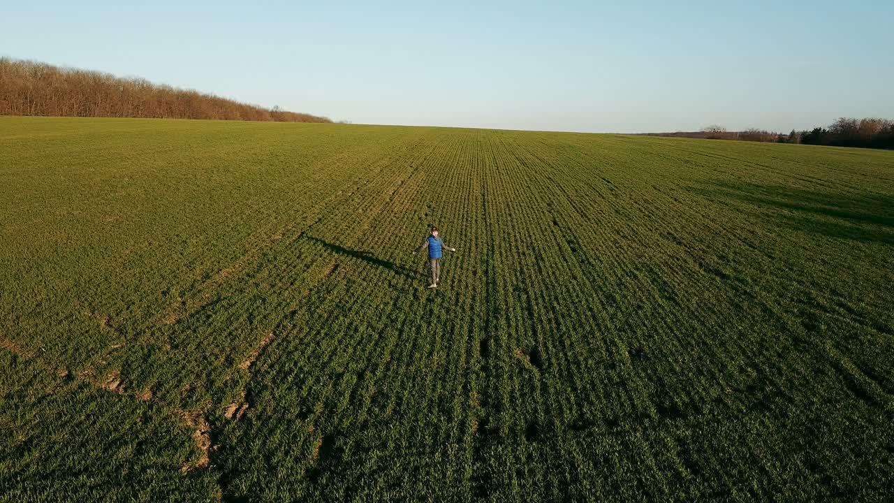 Bambino carino che corre e si gira su un ampio campo verde in primavera. Un bambino piccolo in tuta sportiva che gioca all'aperto su uno sfondo naturale. Vista aerea.