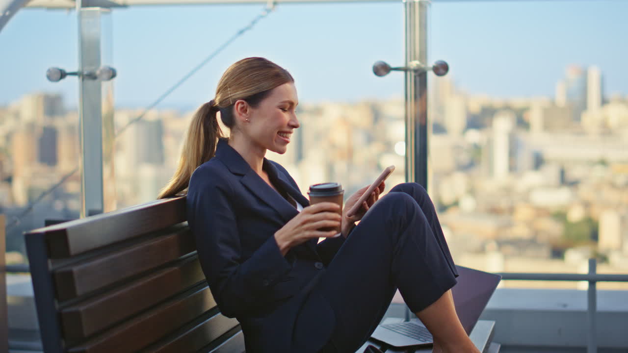 Forretningsmedarbejder browser på smartphone på terrassen. Smilende kvinde drikker kaffe.