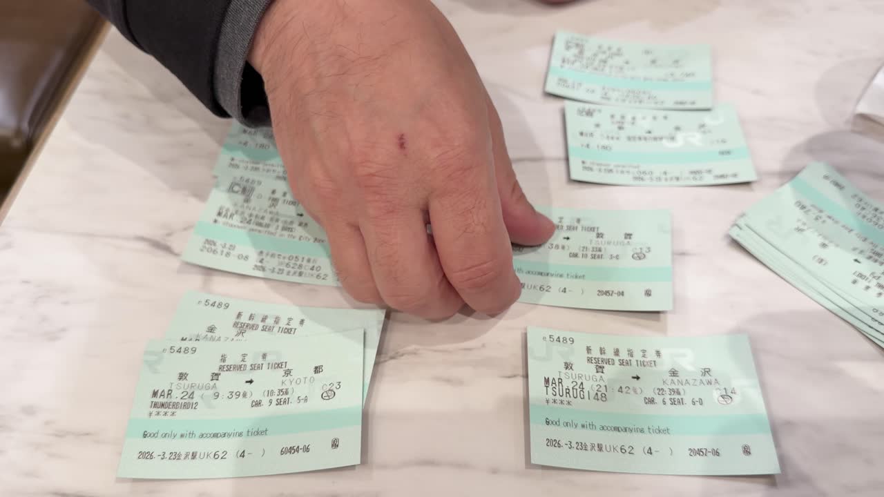 Primo piano di mani che smistano numerosi biglietti verdi del treno su una superficie di marmo
