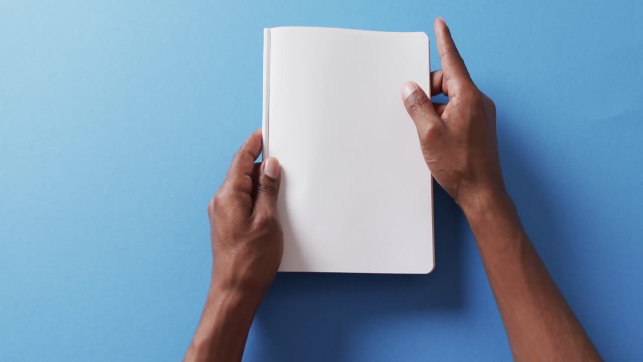 Close up of hand leafing through book with copy space on blue background in slow motion