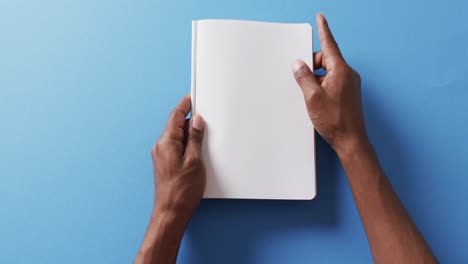 close up of hand leafing through book with copy space on blue background in slow motion