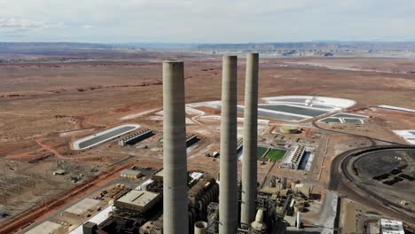 a drone shot of the “navajo generating station”, a massive coal-fired power plant and industrial complex with tall stacks, in the middle of the desert of the navajo nation, located near page, arizona