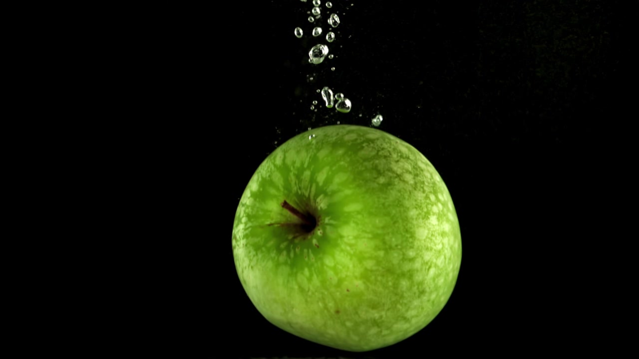 Grønt æble falder ned i vand i slowmotion