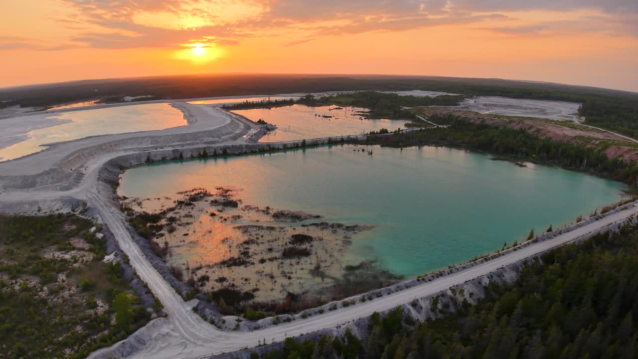 Aerial drone view of a flooded quarry at sunset with reflective water, rocky edges, and surrounding forest