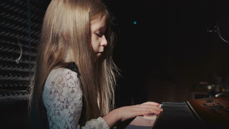 child takes long hair out of face sitting at synthesizer. pretty schoolgirl in lacy blouse prepares to play digital piano in music center. little musician