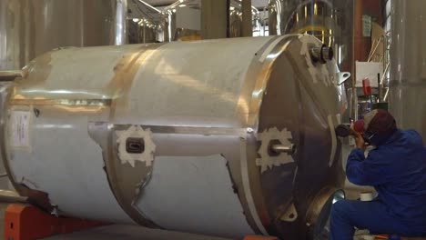 worker repairing a large stainless steel tank in a brewery