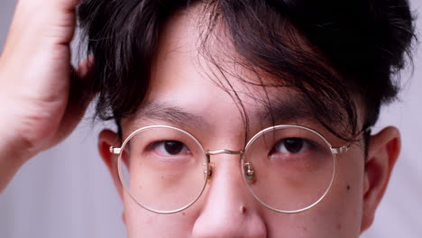 Close-up-Asian-man-with-glasses-and-healthy-good-hair-looking-to-the-camera-and-spoiling-himself-by-tidying-his-hair