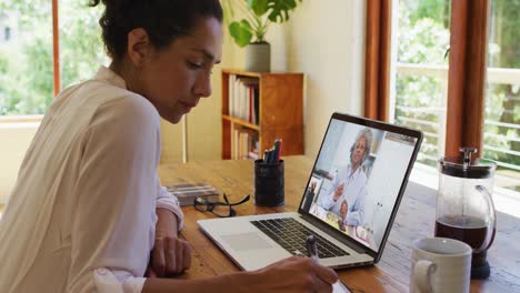 Afroamerikanische-Frau-Macht-Sich-Notizen,-Während-Sie-Zu-Hause-Einen-Videoanruf-Auf-Dem-Laptop-Führt