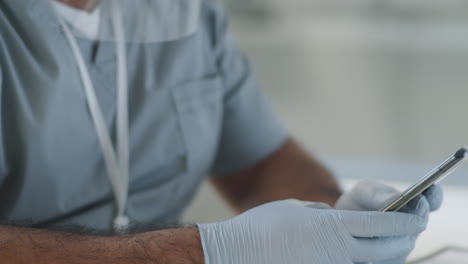 doctor in face shield and mask using smartphone at work