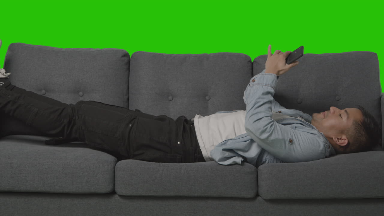 소파에 누워 재채기를 하고 녹색 스크린을 배경으로 휴대폰을 보는 젊은 남자