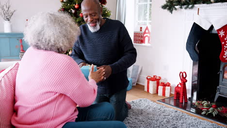 senior black man giving a christmas gift to his partner, then they hug each other, front view