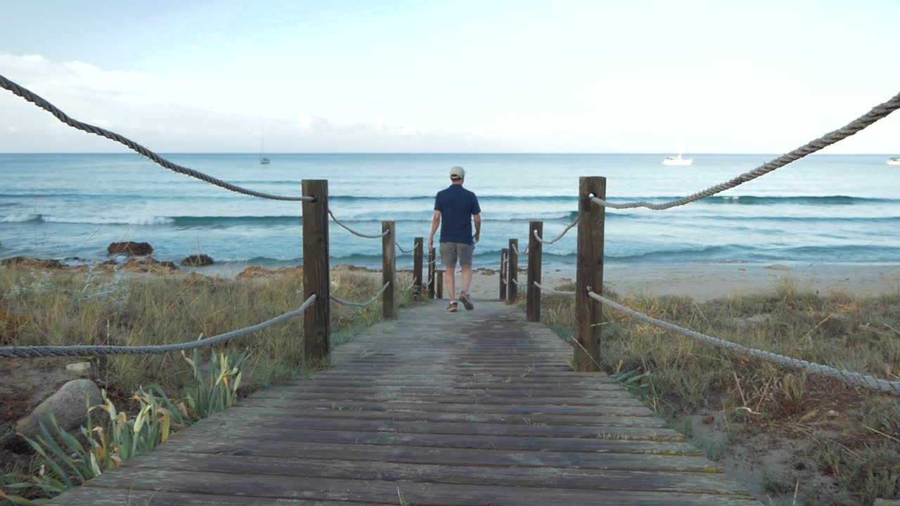 스포츠를 하기 위해 새벽에 해변으로 가기 위해 나무 판자로 만든 길을 가는 남자