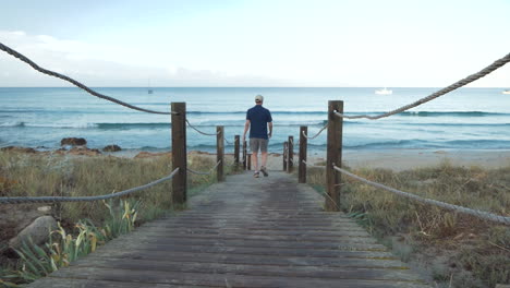 hombre tomando un camino hecho de tablas de madera para ir a la playa al amanecer a hacer algunos deportes